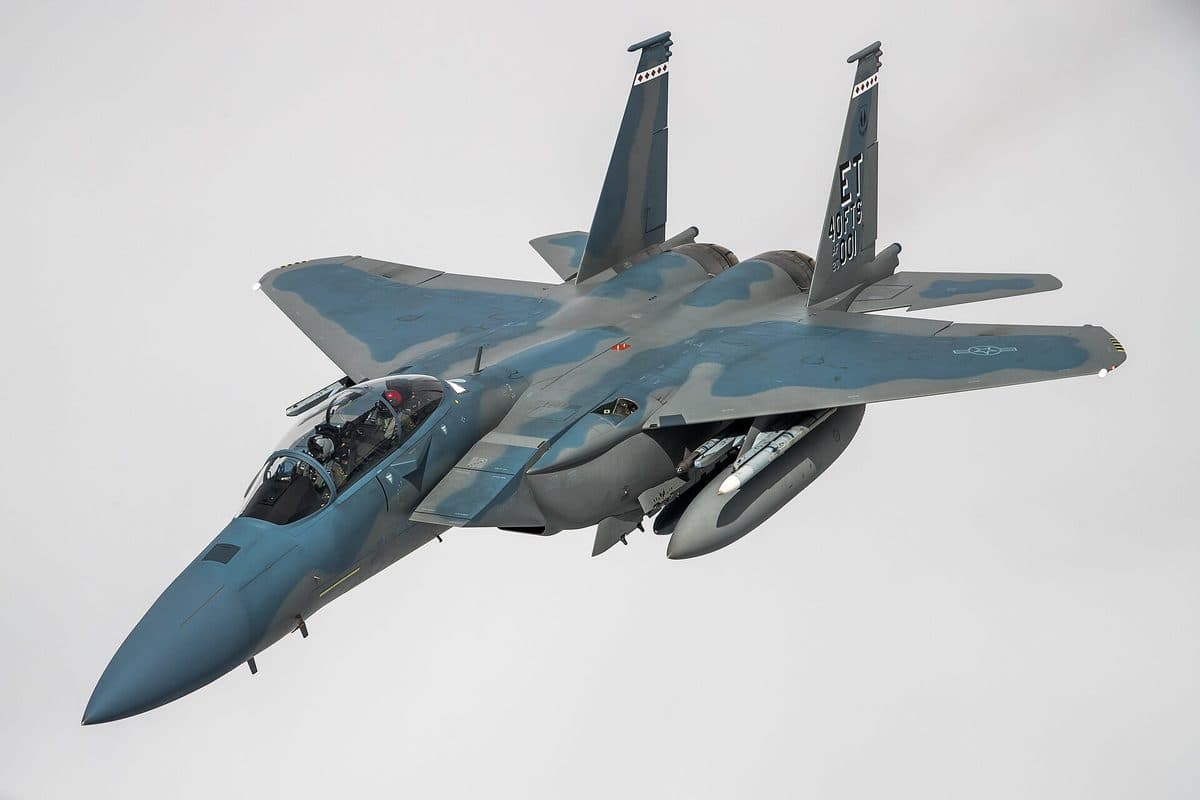 F-15E Strike Eagle loaded with ordnance flying over desert terrain