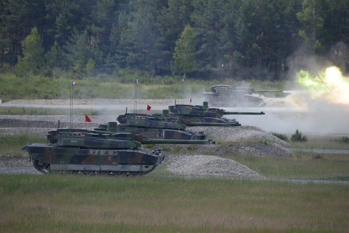 French Leclerc main battle tank moving at speed across desert terrain kicking up a dust plume