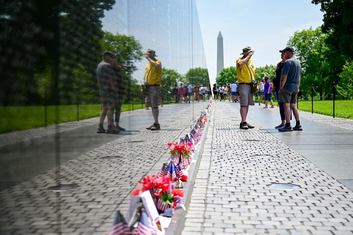 Visitors walk along the Vietnam Veterans Memorial Wall in Washington, D.C., with names of the fallen reflected in the black granite