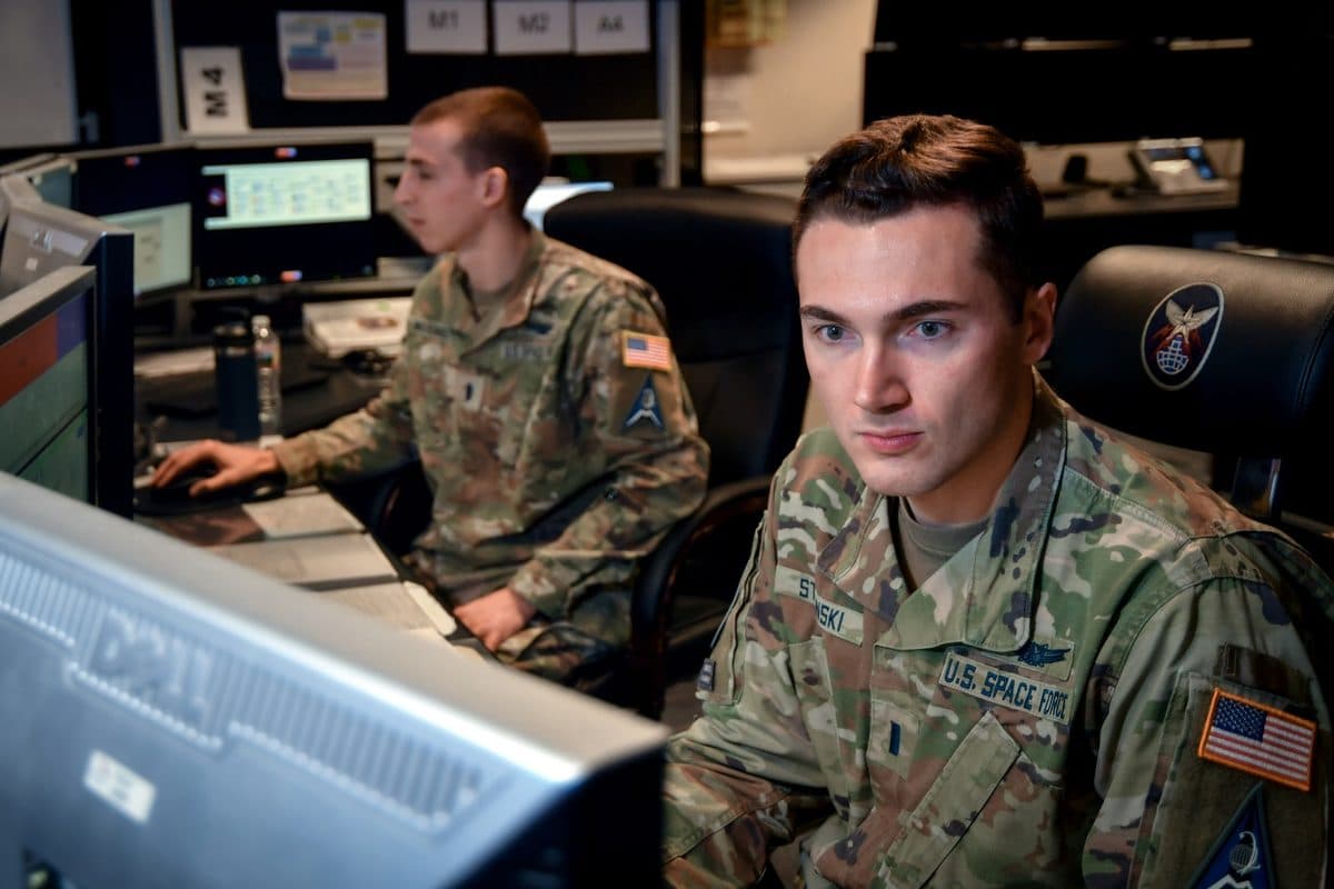 KH-11 style reconnaissance satellite rendering in low Earth orbit above cloud-covered terrain