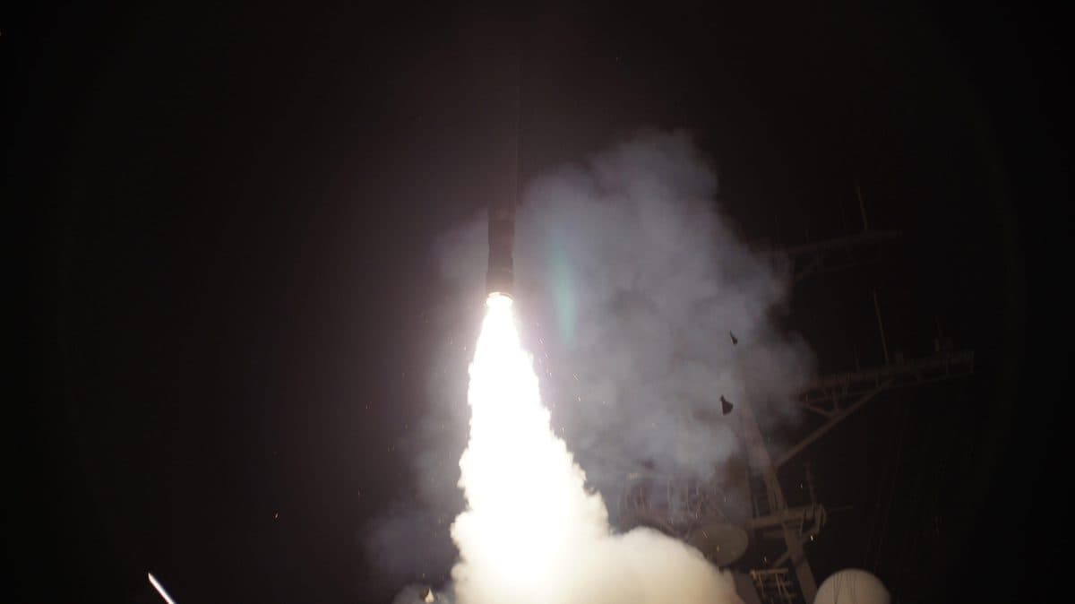 Tomahawk cruise missile launching from a warship's vertical launch system with booster ignition visible