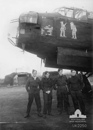 Lancaster bomber with ground crew posing beneath the nose, bomb mission tallies visible on fuselage