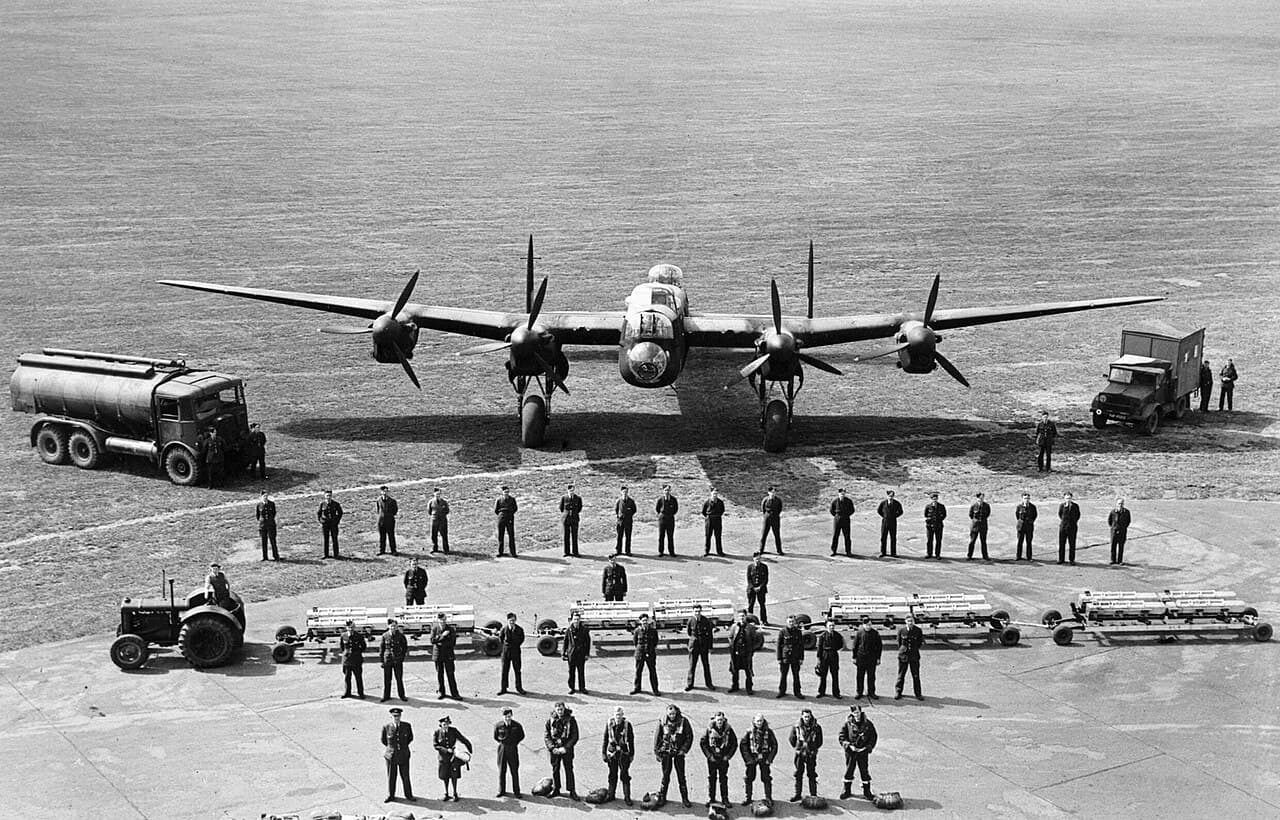 Lancaster bomber with full crew and bomb load displayed in front, squadron photo