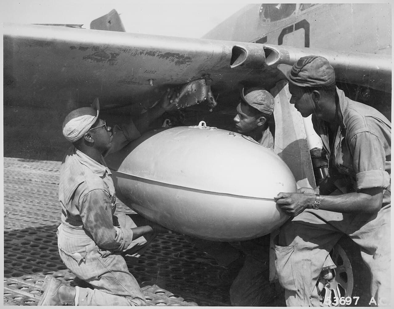 Ground crew loading an external drop tank onto a P-51 Mustang at an airfield in Italy