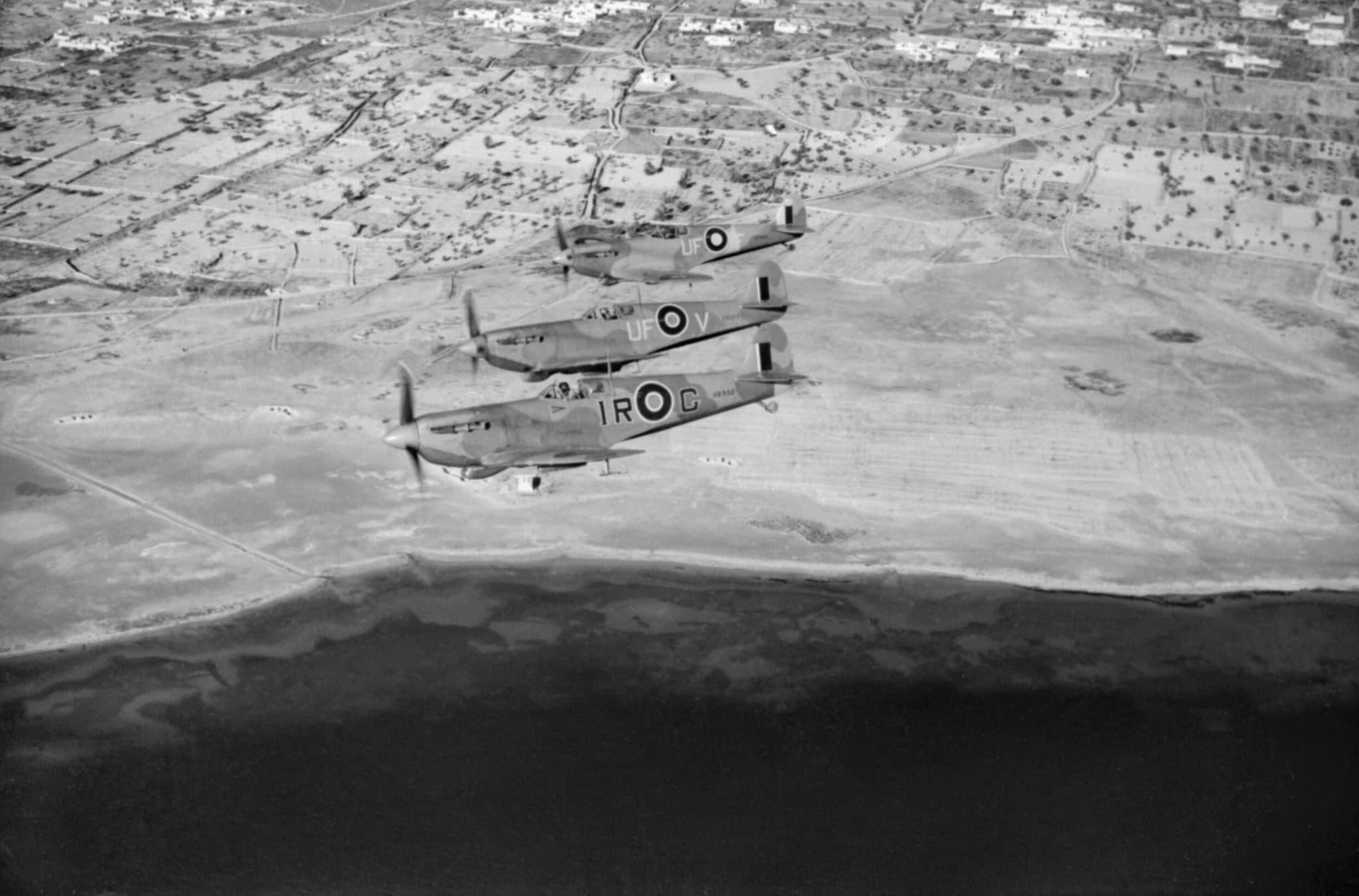 Three RAF Spitfires flying in formation over a coastline