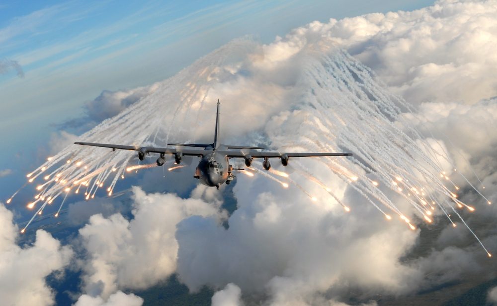 AC-130 gunship deploying defensive flares in flight over clouds