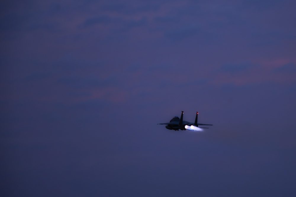 F-15E Strike Eagle in flight at twilight with glowing afterburner exhaust