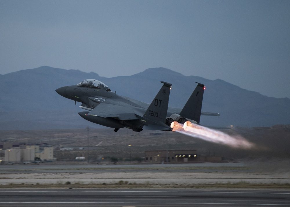 F-15E Strike Eagle taking off with twin afterburners lit and mountains in the background