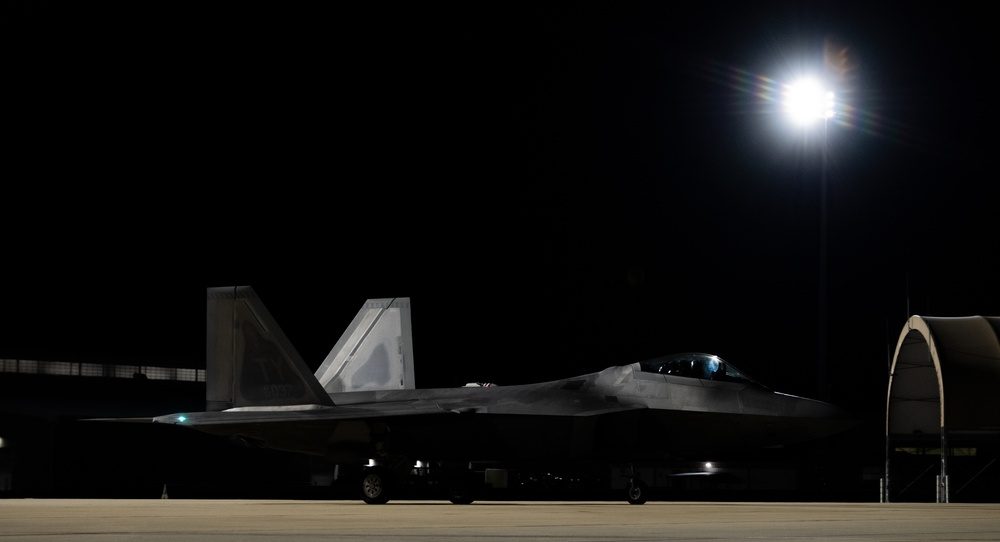 F-22 Raptor photographed during night operations, with the aircraft's silhouette visible against a dark sky