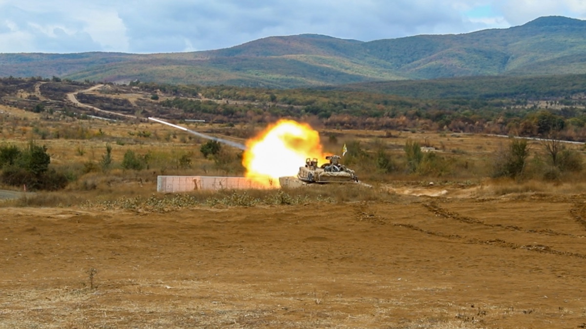 M1A2 SEPv3 Abrams tank in desert tan livery during a gunnery exercise, with Trophy active protection system visible on the turret sides
