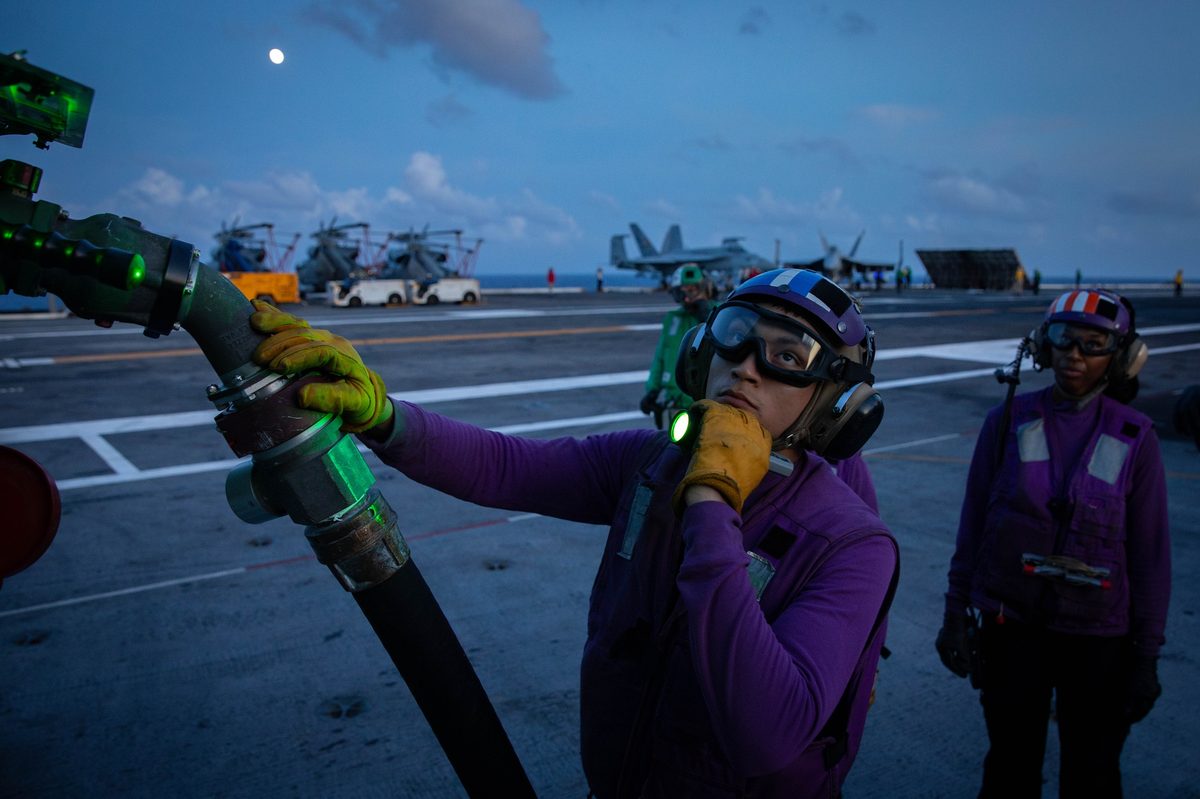 Flight deck crew conducting fueling operations during nighttime carrier operations