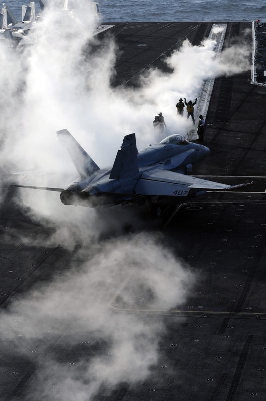 F/A-18 Hornet launching from an aircraft carrier with steam rising from the catapult track