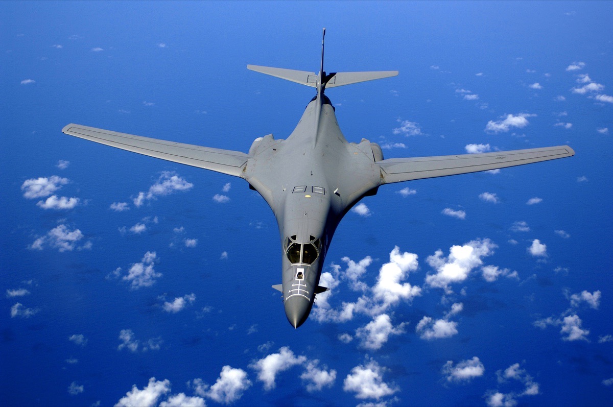 B-1B Lancer supersonic bomber in flight with its variable-geometry wings swept back, viewed from below against a blue sky