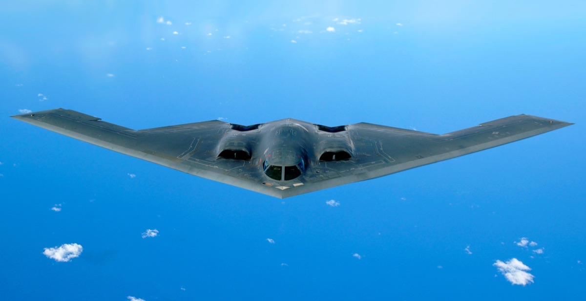 B-2 Spirit stealth bomber in flight during an air show, showing its distinctive flying wing planform against a blue sky