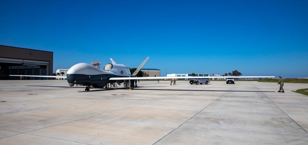 MQ-4C Triton unmanned aerial vehicle on a runway, showing its high-aspect-ratio wings and sensor dome beneath the fuselage
