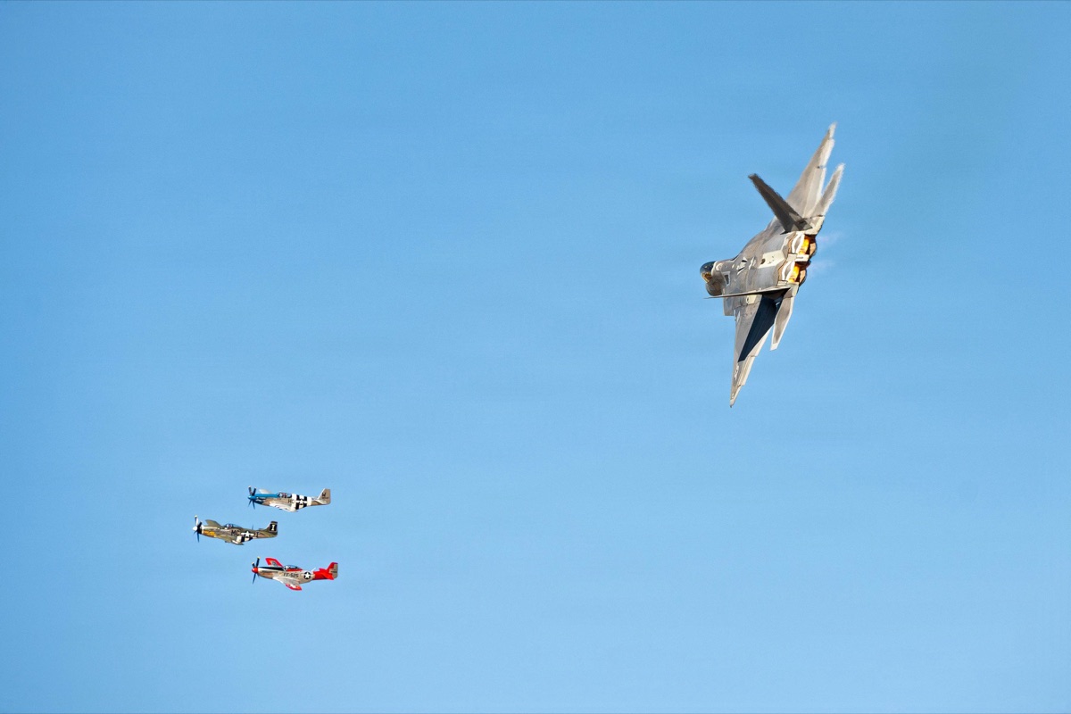 F-22 Raptor performing a high angle of attack maneuver alongside P-51 Mustang fighters in a heritage flight demonstration