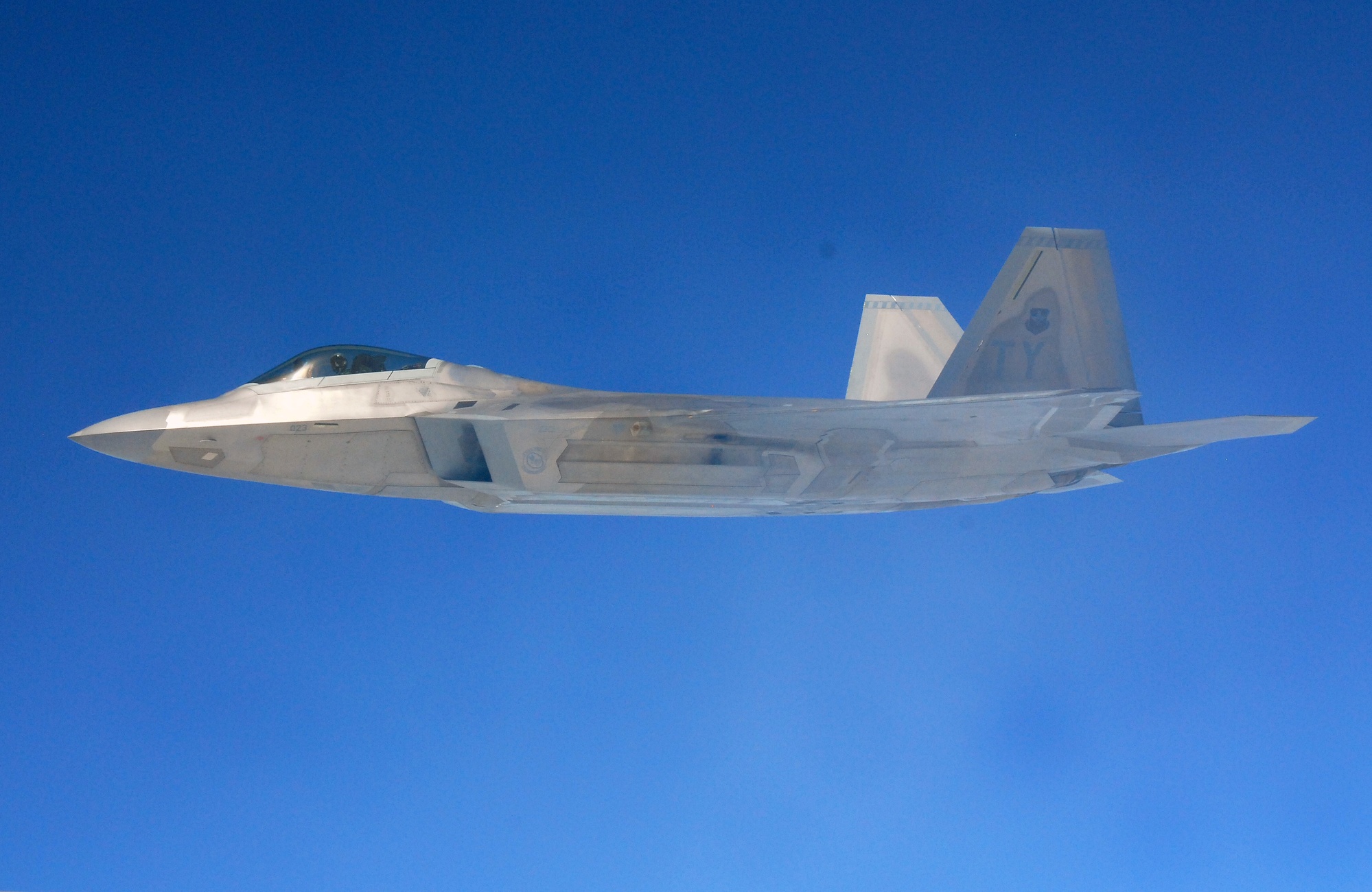 F-22 Raptor in flight showing its angular stealth profile against a blue sky