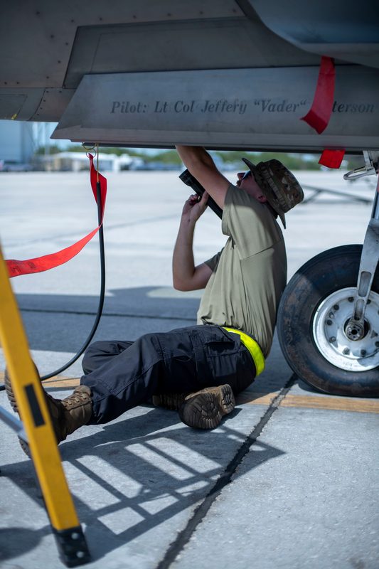 Air Force crew chief inspecting the underside of an F-22 Raptor during maintenance at Naval Air Station Key West