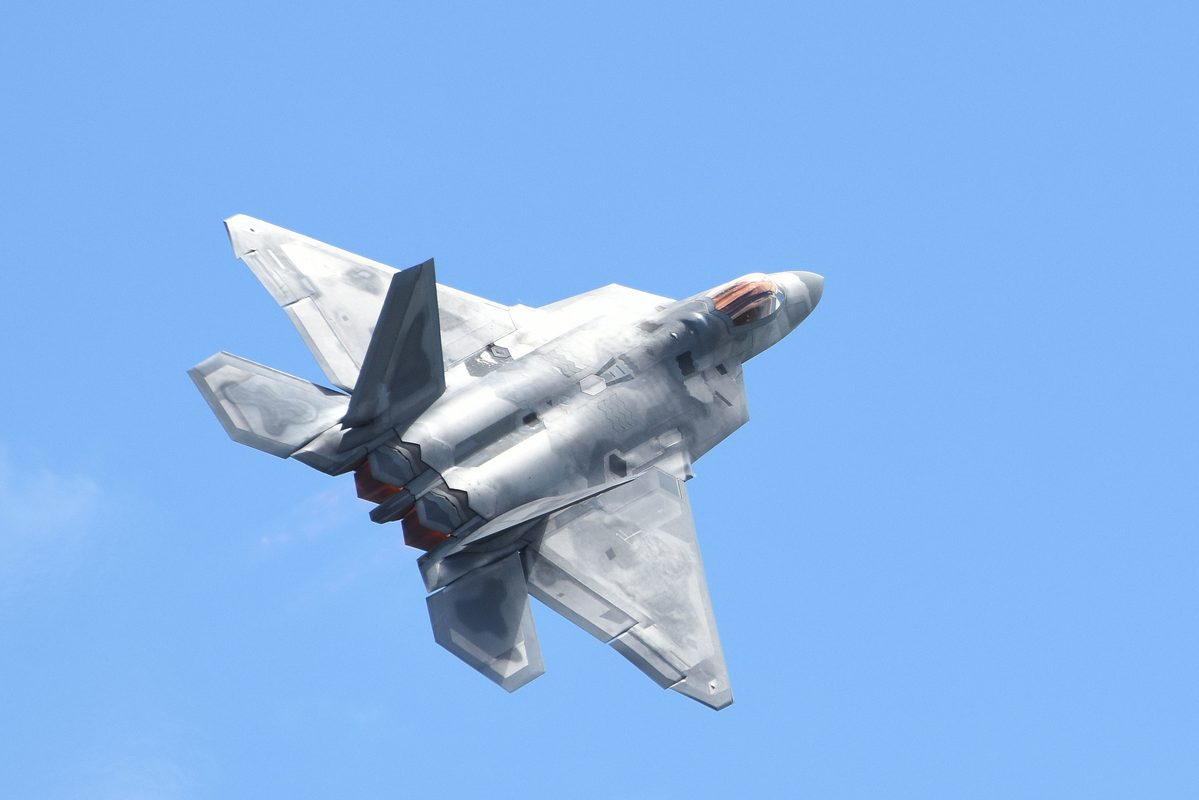 F-22 Raptor maneuvering in flight with afterburner visible against blue sky
