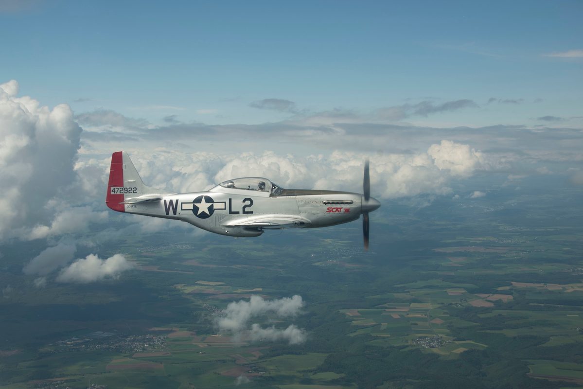 P-51 Mustang with red tail markings in flight over countryside