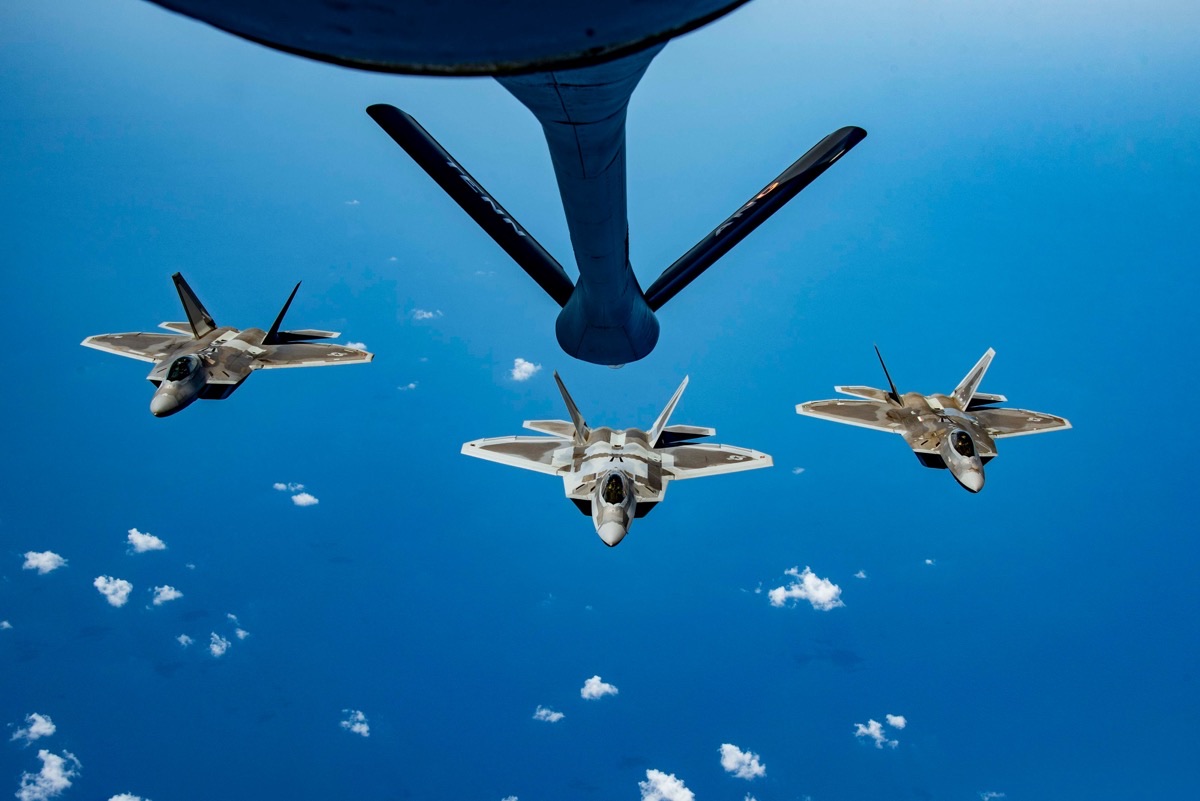 Three F-22 Raptors in formation behind a KC-135 Stratotanker refueling boom during aerial refueling