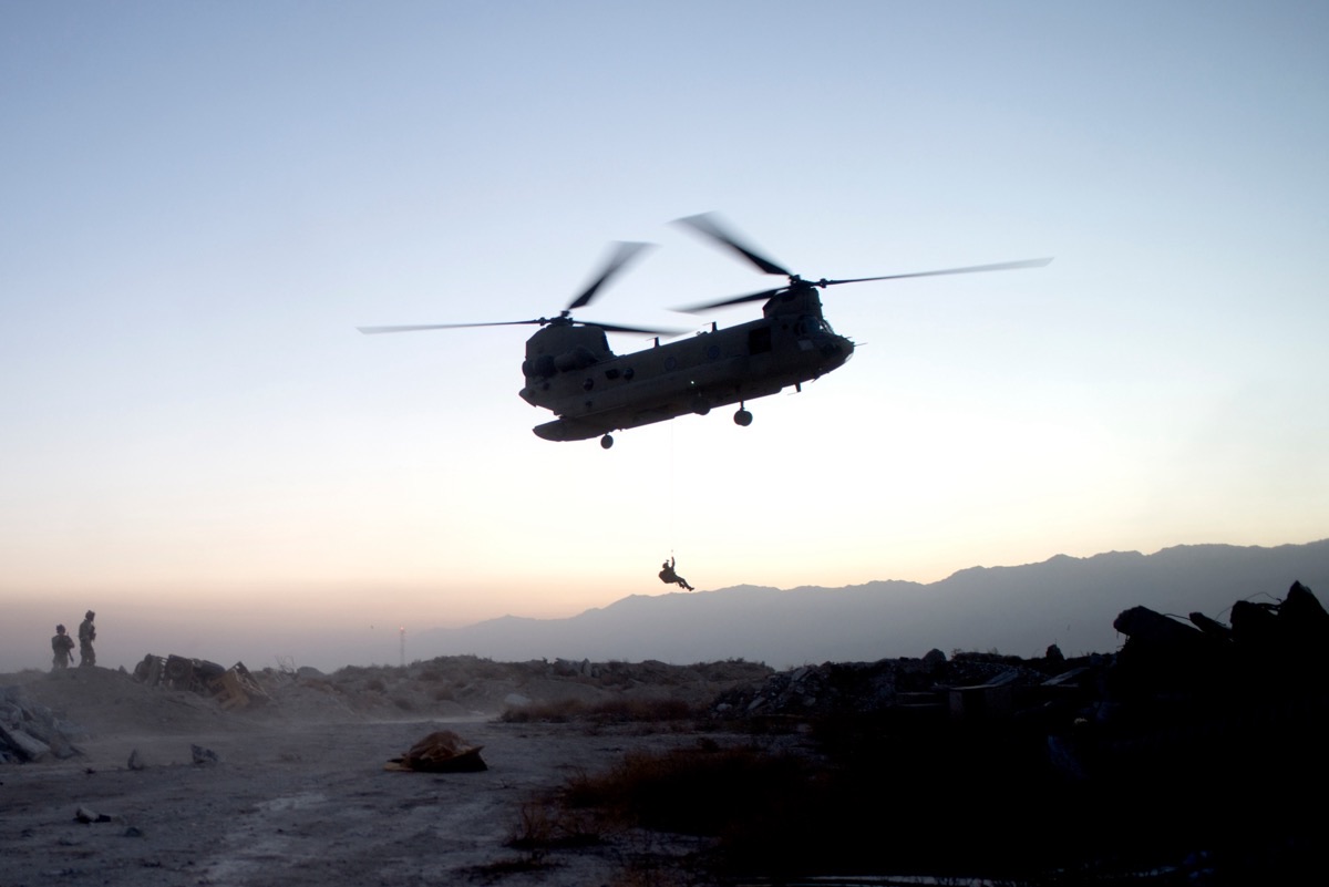 Pararescueman being hoisted from a helicopter during a combat search and rescue operation at dusk in Afghanistan