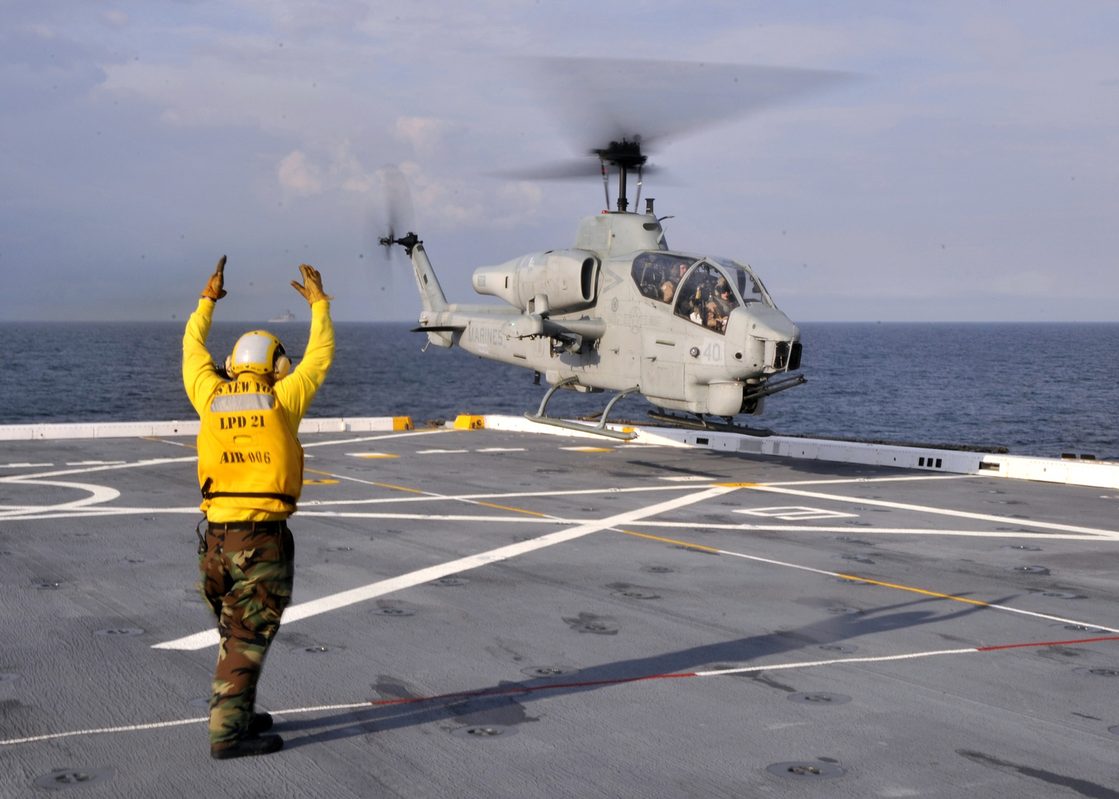 AH-1 Cobra attack helicopter landing on a naval vessel showing its narrow tandem-seat fuselage