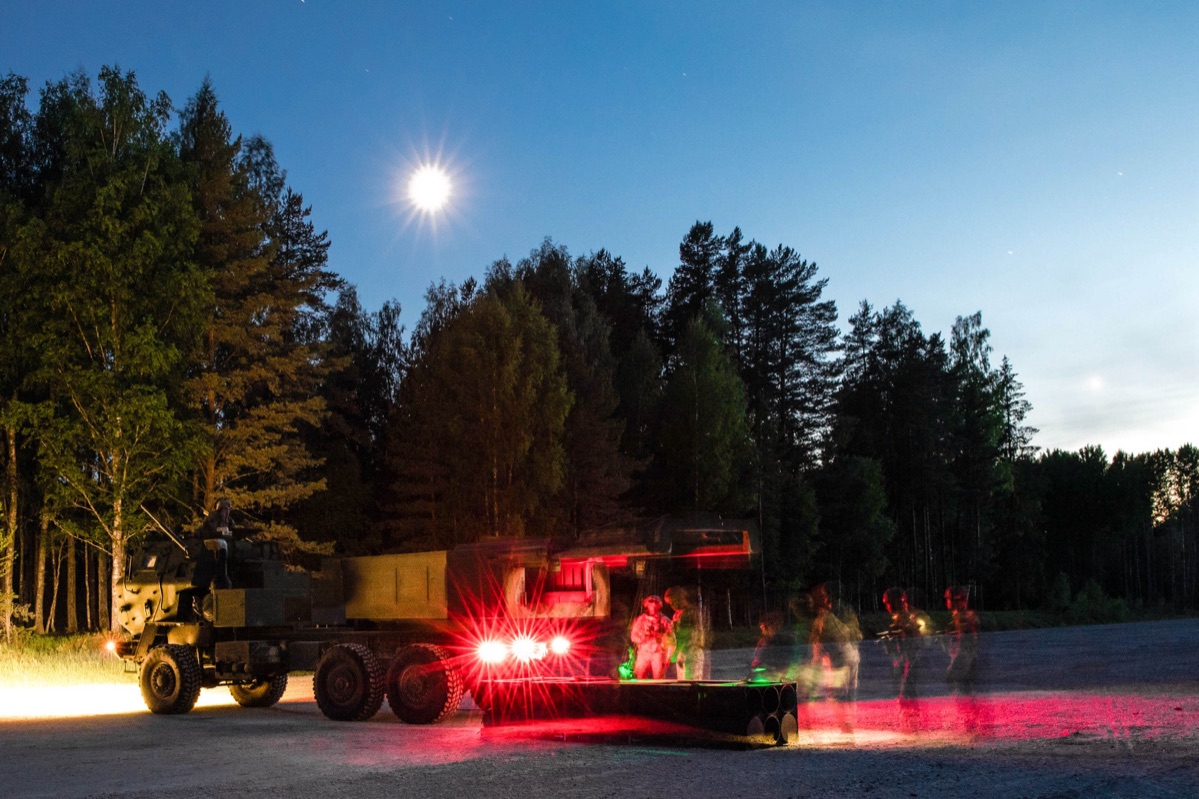 HIMARS launcher firing at night with soldiers operating the system, rocket exhaust illuminating the scene
