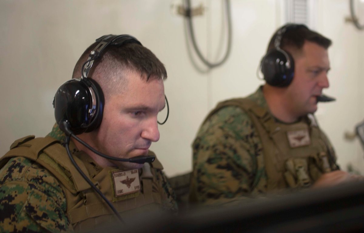 U.S. Marine Corps officers reviewing tactical information on multiple screens inside a Tactical Air Control Center during operations