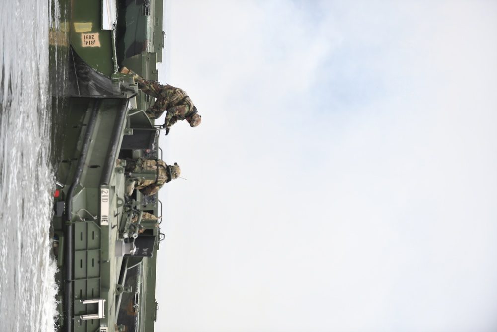 U.S. Army combat engineers in tactical gear working on bridge components during a field exercise, with military vehicles visible in the background