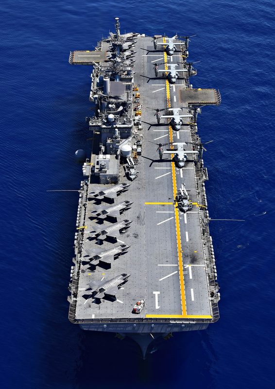 Aerial view of a Wasp-class amphibious assault ship at sea with F-35Bs, V-22 Ospreys, and helicopters on deck