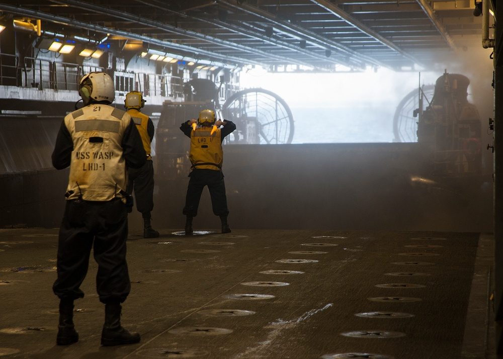 USS Wasp well deck interior with sailors directing a landing craft air cushion